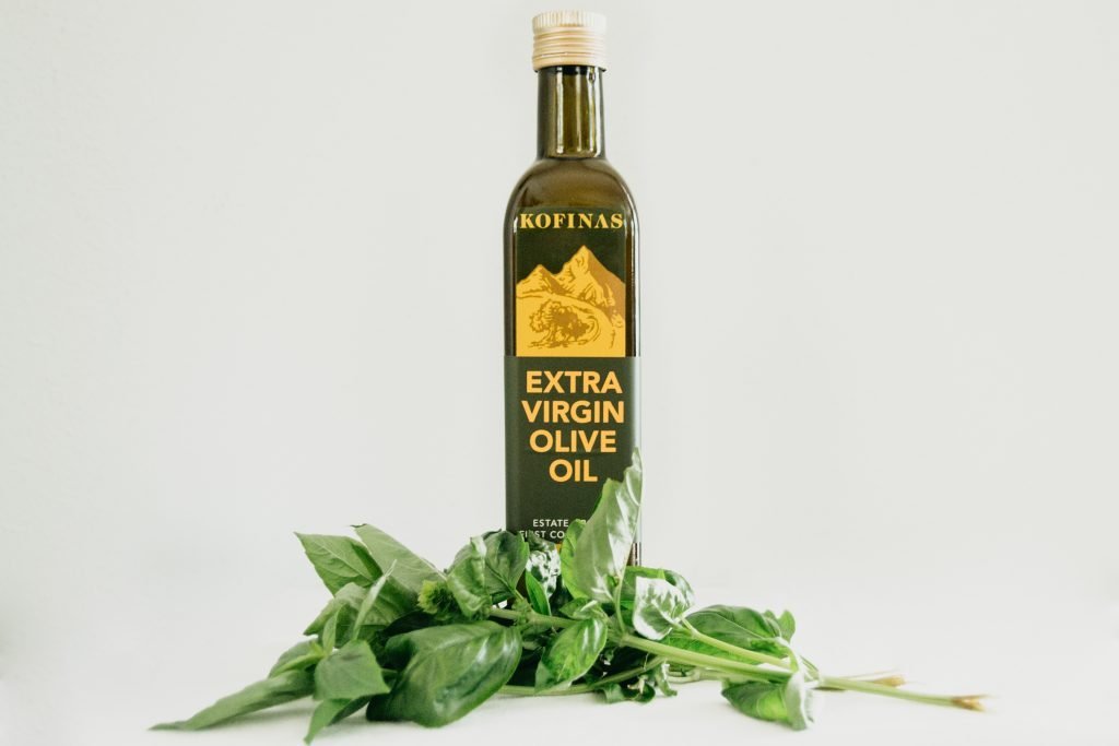 A bottle of extra virgin olive oil from the Kofinas estate, with a basil stalk resting in front.