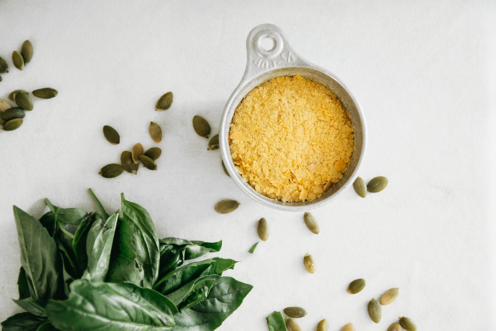 Nutritional yeast in a 1/3 cup measuring utensil, alongside other ingredients for vegan basil pesto.