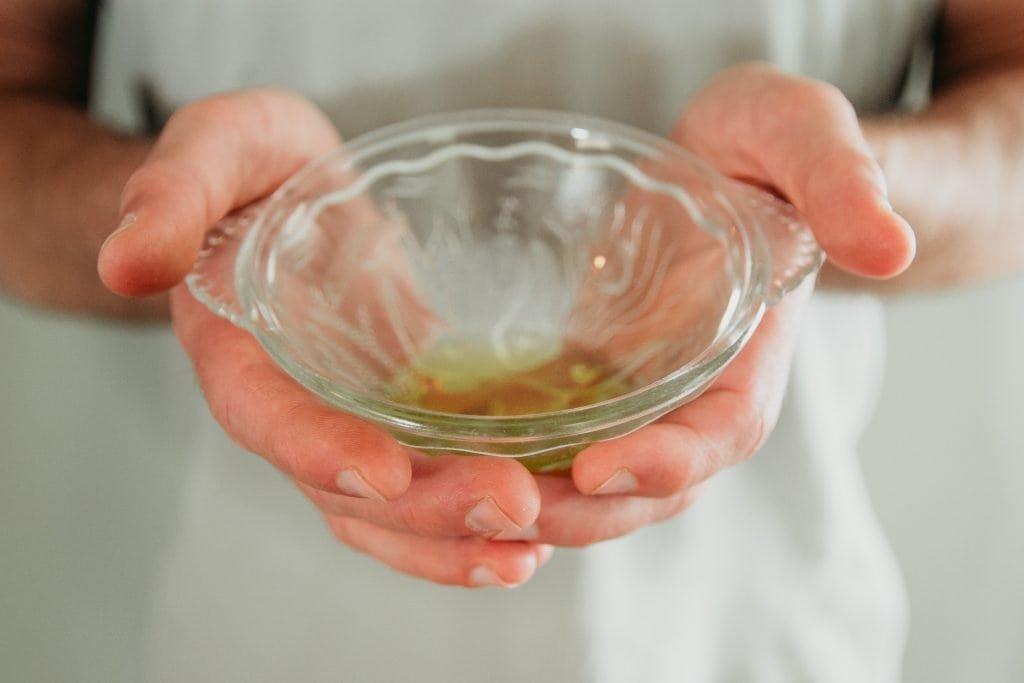 Hands hold olive oil in a petite glass dish.