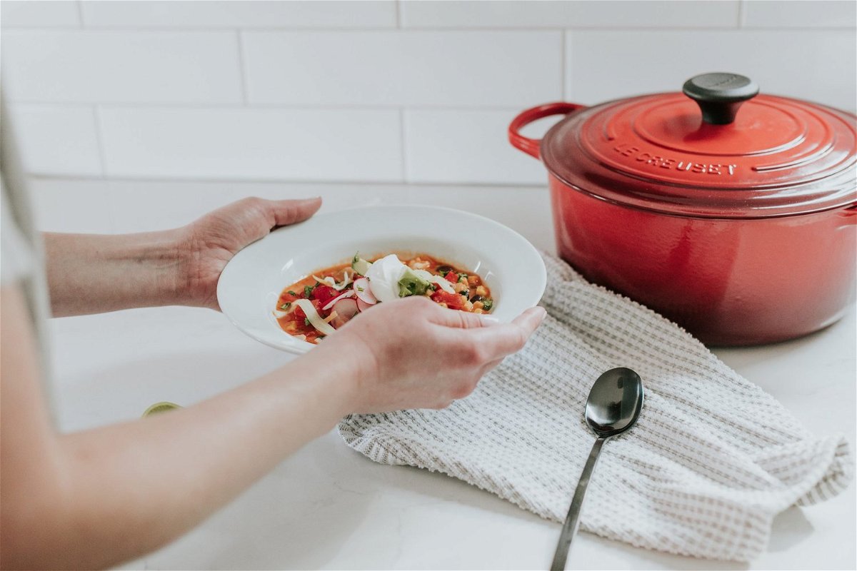 red dutch pot and a woman holding a white plate with food near it