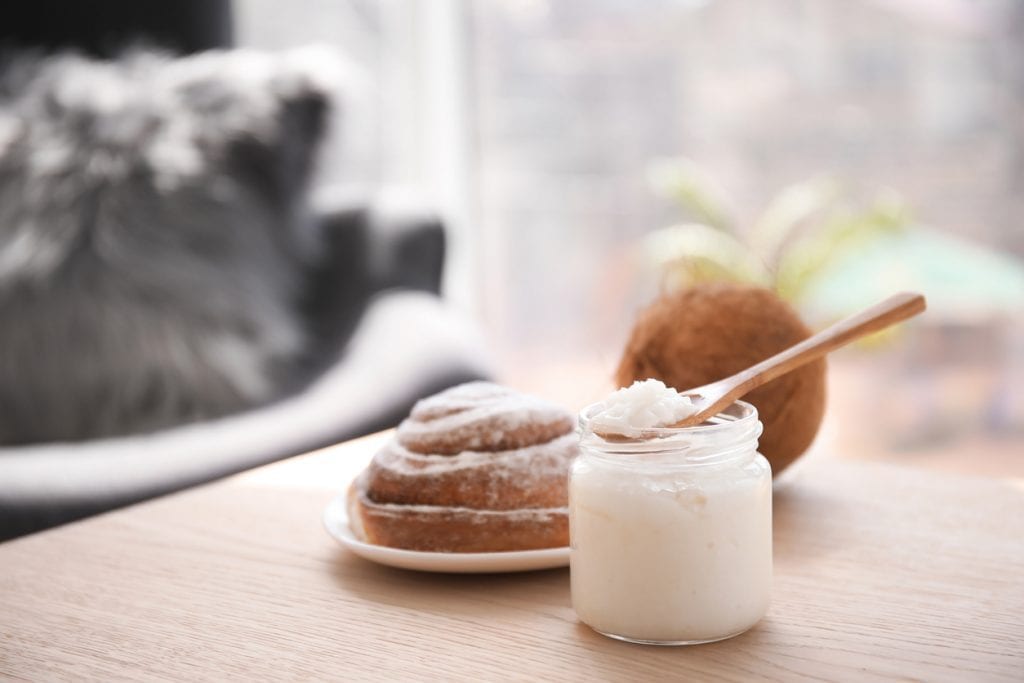 Wooden spoon and jar with coconut oil on table. Healthy cooking