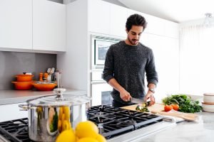 man cuting vegetables on a wooden cutting board in a white kitchen