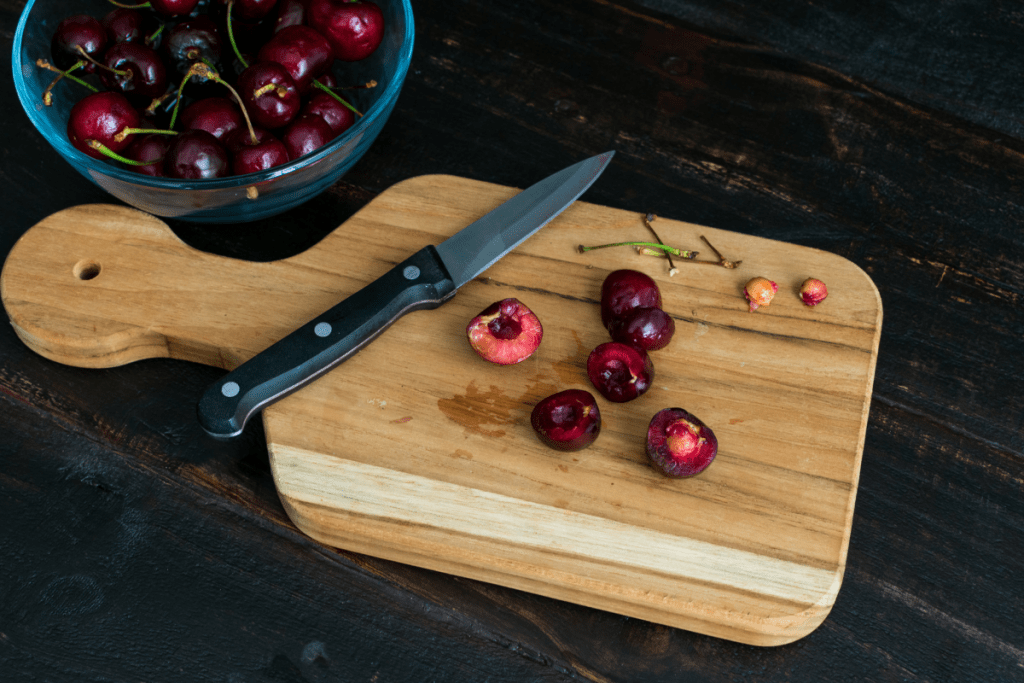 a paring knife rests on a cutting board with cherries