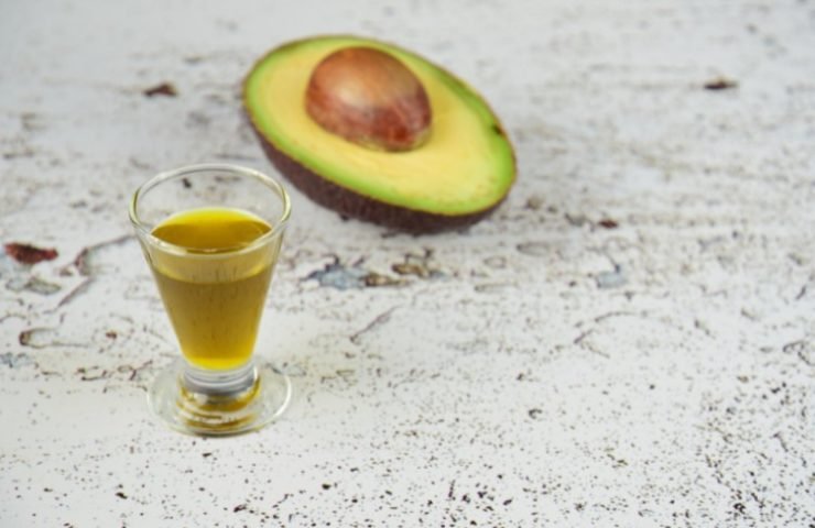 avocado oil in a glass next to an half open avocado