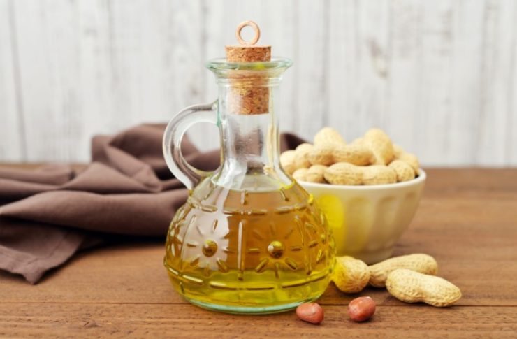 peanut oil in a jug next to a small bowl of peanut on a wooden table