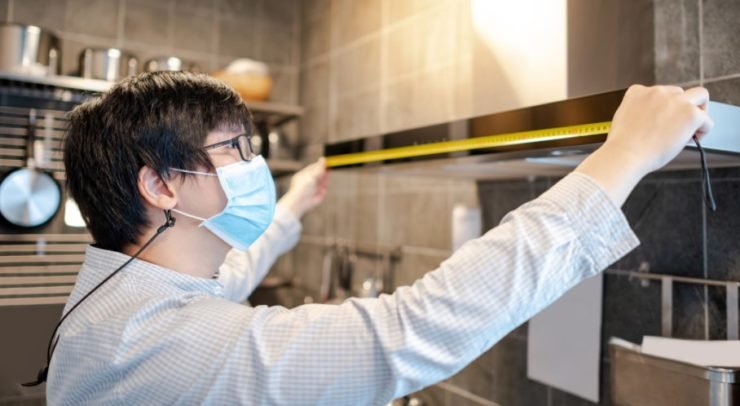 Asian man using tape measure on kitchen hood in showroom