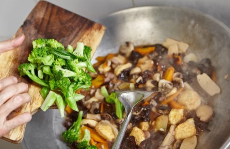 chef adding broccoli in a wok 