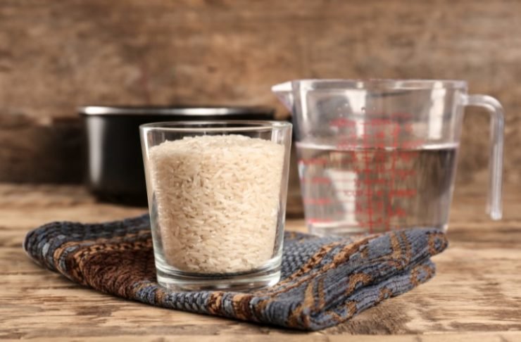 Glass of Rice and Measuring Jug with Water on Wooden Table