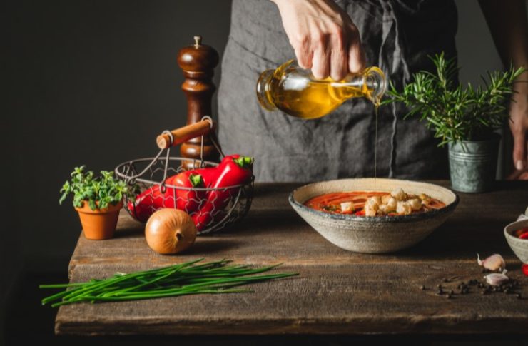 Chef adding olive oil in red pepper soup pot