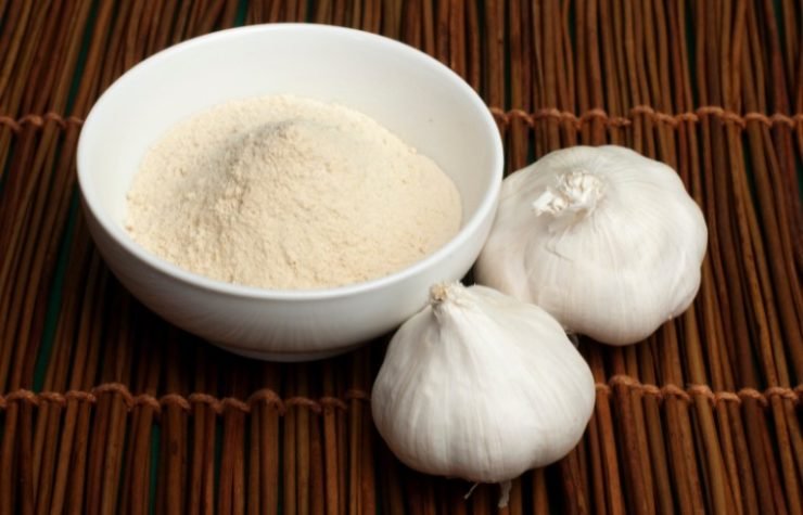 fresh garlic next to a bowl with garlic powder