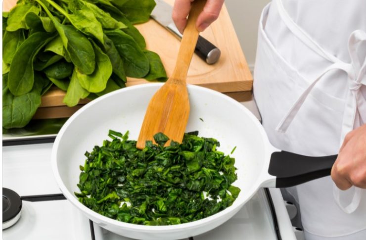 cooking spinch in a white pan