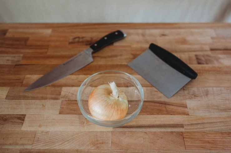 knife , bench scraper and onion in a bowl