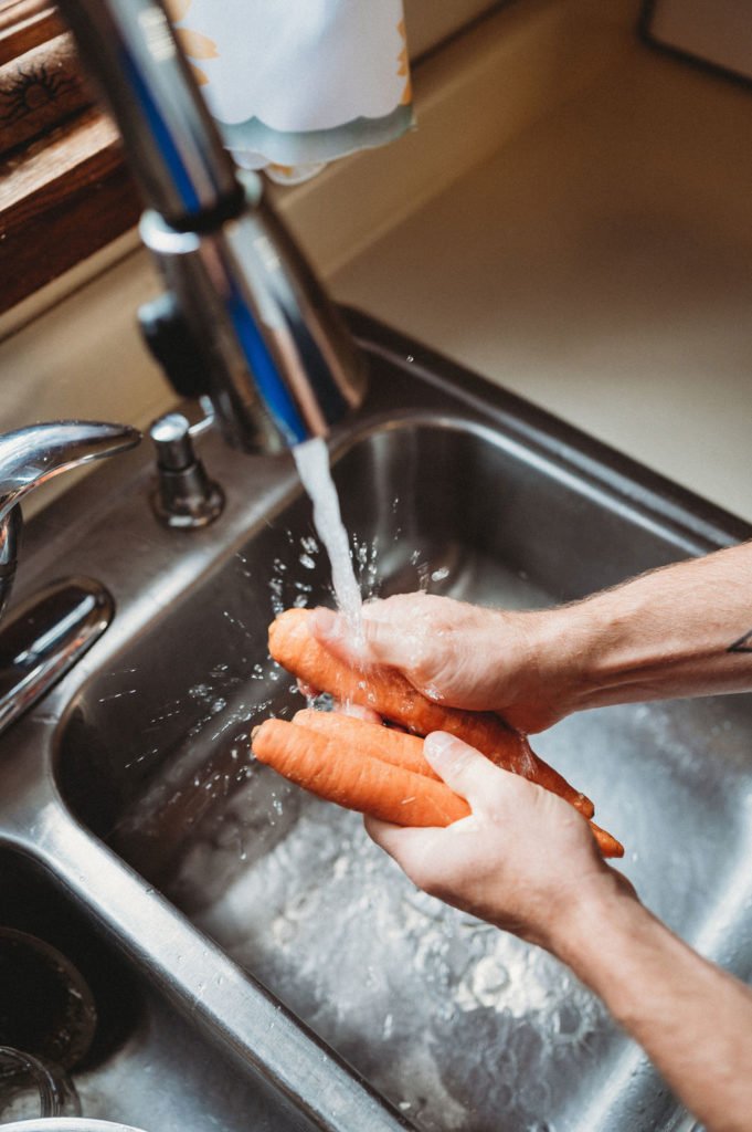person washing carrots above the sink