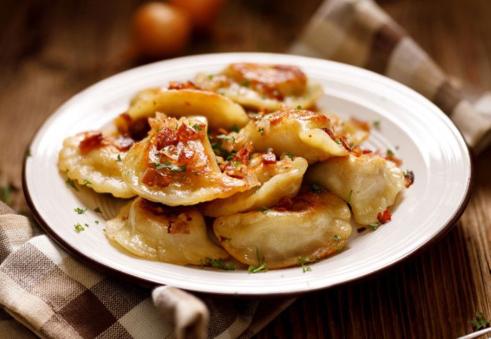 Fried dumplings stuffed with cabbage and meat sprinkled with bacon greaves and chopped parsley on a white plate