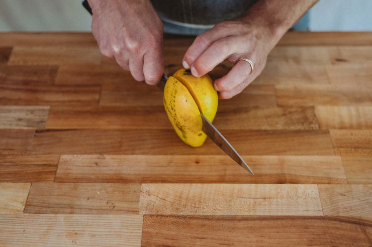 person cutting half of a mango