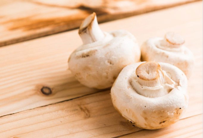 Three White Mushrooms on Beige Wooden Table