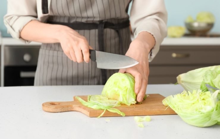 Woman Cutting Iceberg Lettuce on Table in Kitchen
